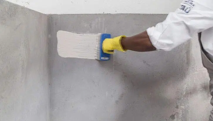 mão de profissional com luva segurando aplicador e aplicando pintura a base de cal e tinta em pó em alvenaria estrutural