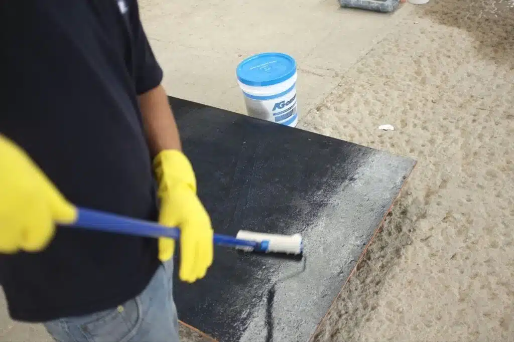 homem segurando rolo para aplicação com luvas amarelas enquanto aplica desmoldante para concreto na fôrma